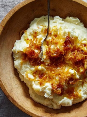 Mashed potatoes with caramelized onions and goat cheese in a wooden bowl.