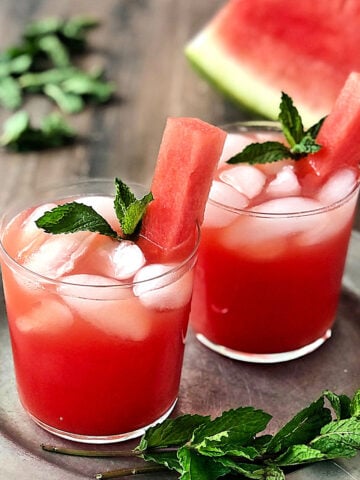 2 glasses of Watermelon Agua Fresca on a silver plate with mint leaves scattered around them.