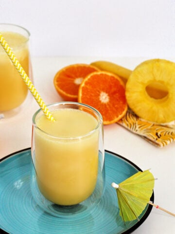 Pineapple banana smoothie on a blue plate with a yellow and white striped straw.