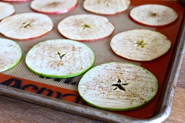 Raw slices of apples dusted with cinnamon on a baking sheet.