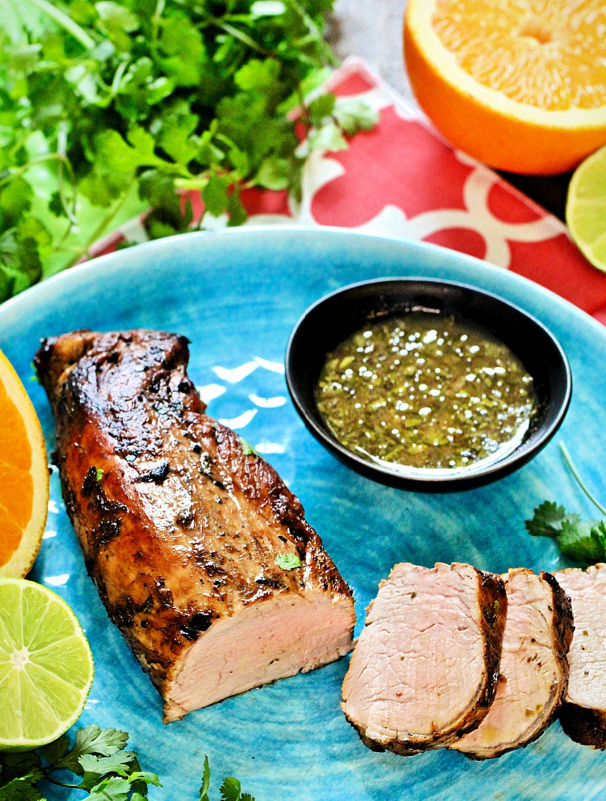 Cuban mojo pork tenderloin on a blue plate with mojo sauce in a black bowl.