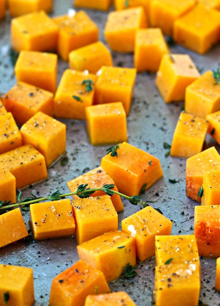 Diced butternut squash on a sheet pan with thyme leaves before cooking.