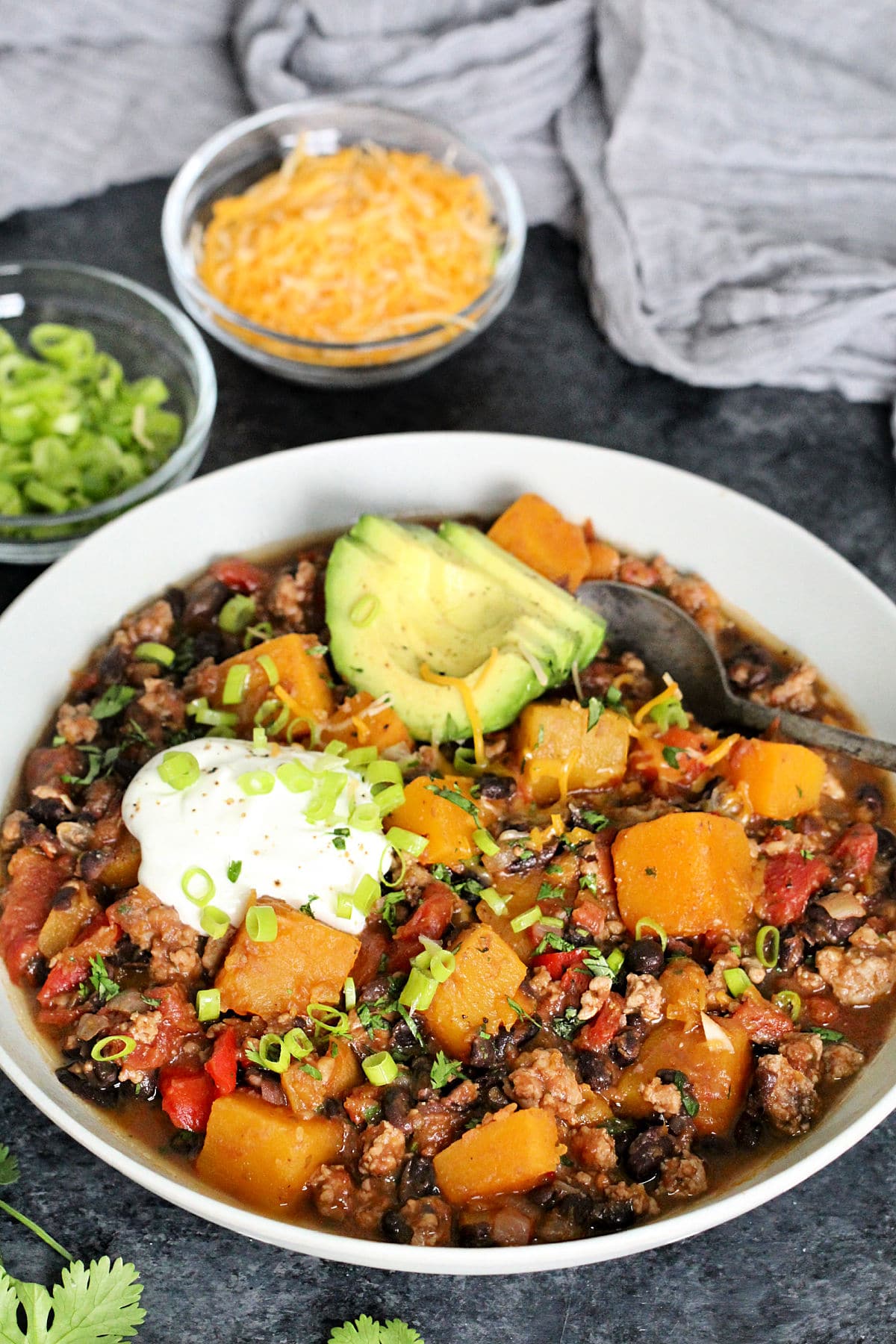 Butternut Squash & Turkey Chili in a white bowl with cheese and scallions in the background
