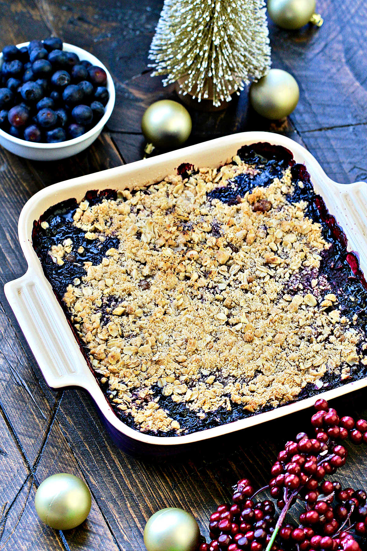 Angled photo of blueberry crisp in a square baking dish with holiday decorations.