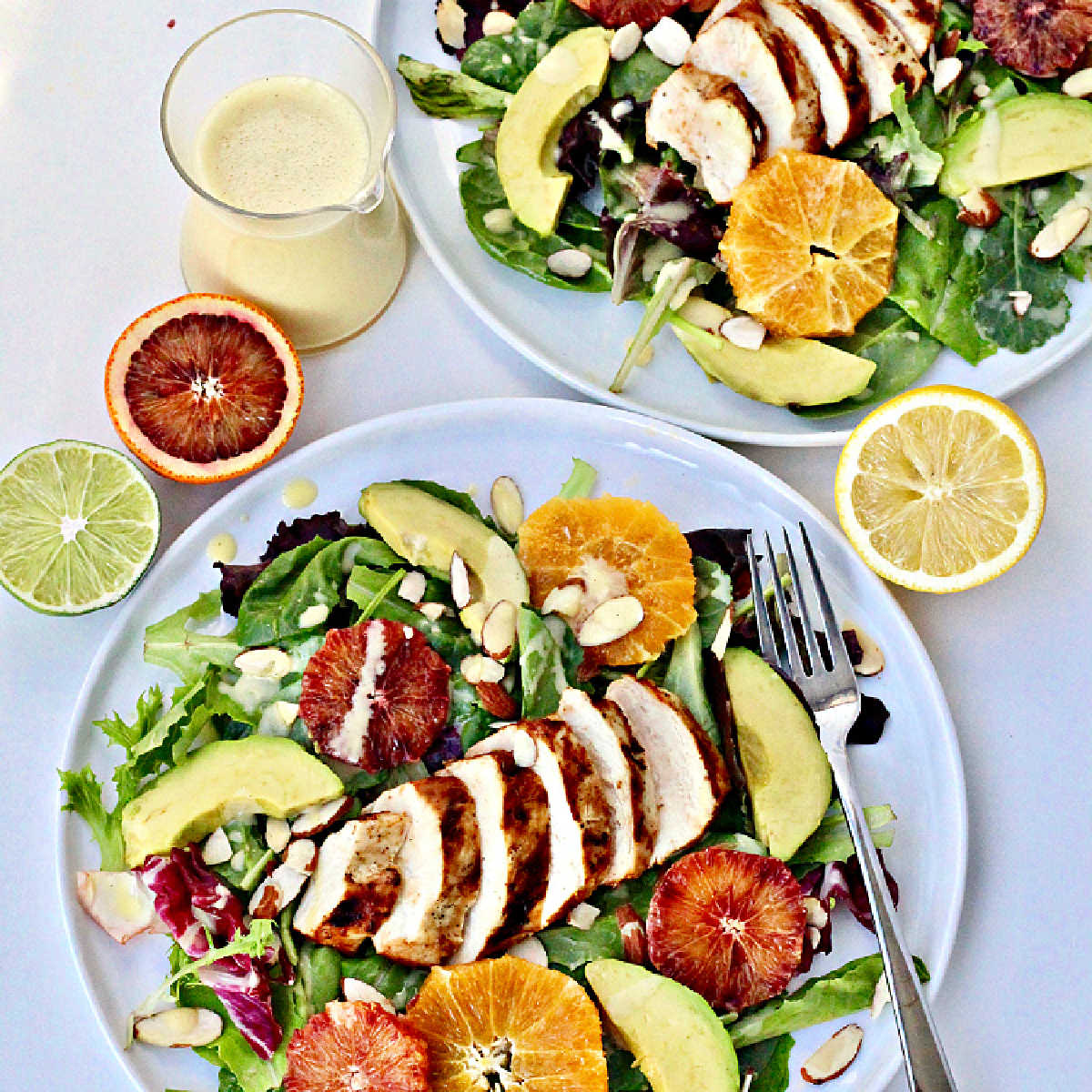 Overhead shot of summer citrus salad on a white plate with halved citrus fruit and dressing on the side.
