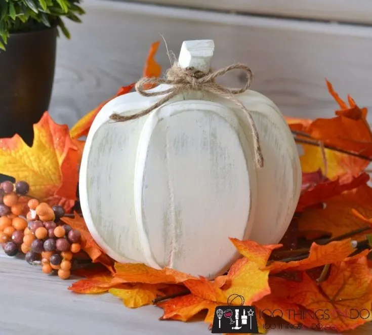 white wooden pumpkin surrounded by fall leaves