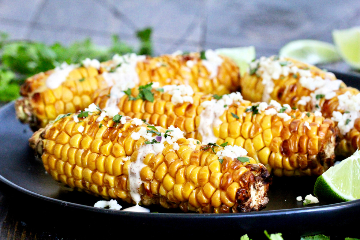 Four pieces of air fryer corn on the cob on a black plate.