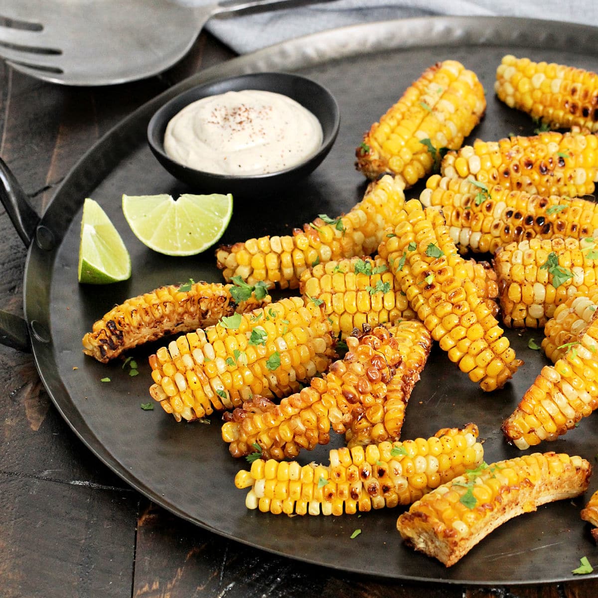 Corn ribs on a bronze platter with lime wedges and Southwest dipping sauce.