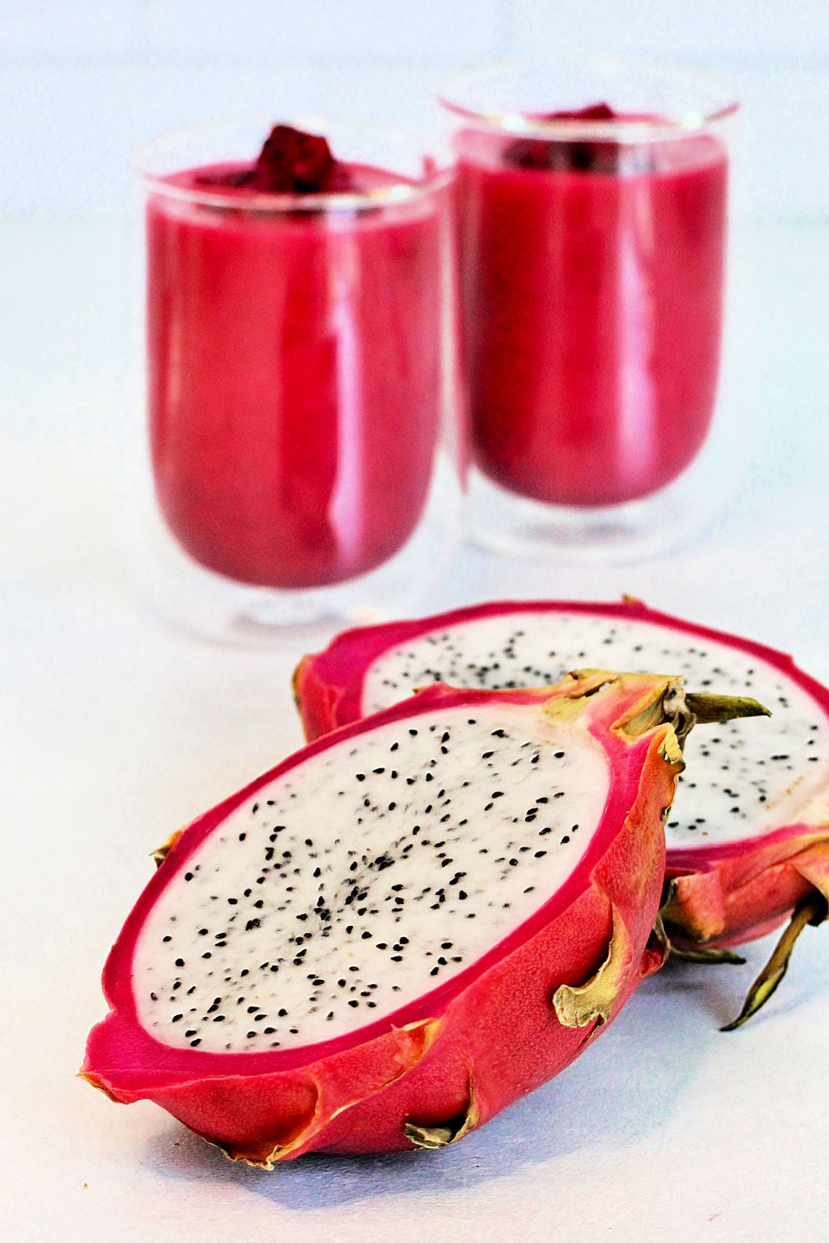 A halved dragon fruit with two dragon fruit smoothies in the background.