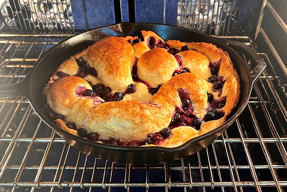 Blueberry Lemon Dutch Baby in cast iron skillet puffing up in the oven.
