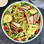 Overhead shot of santa fe salad in a white bowl with a small bowl of dressing on gray board.