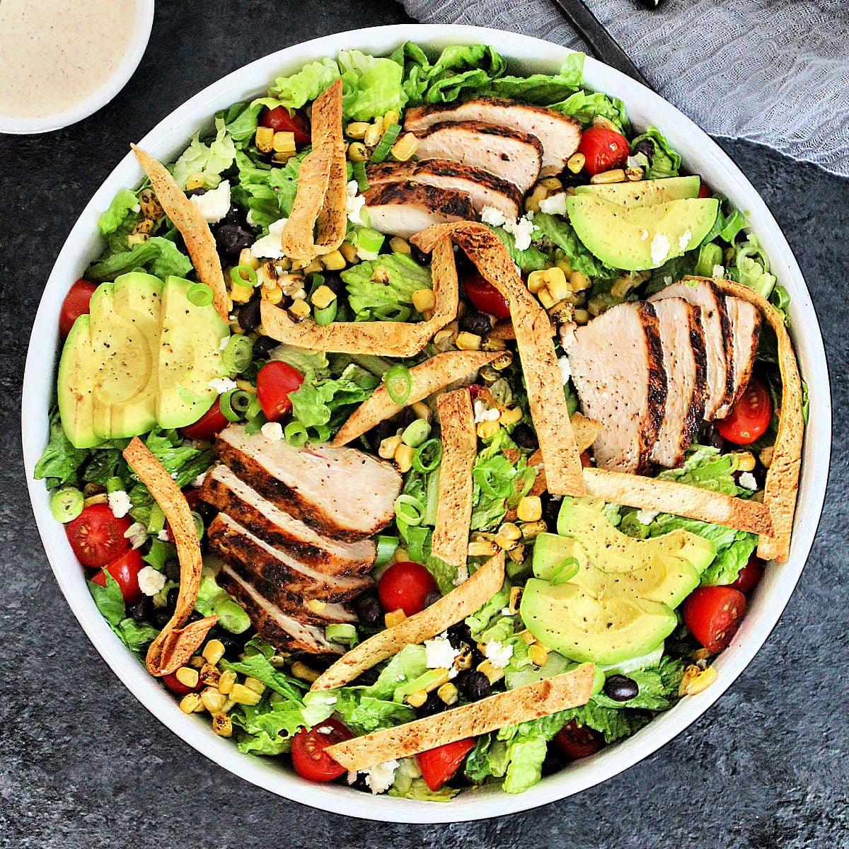 Overhead shot of Santa Fe Salad in a white bowl with a small bowl of dressing on gray board.