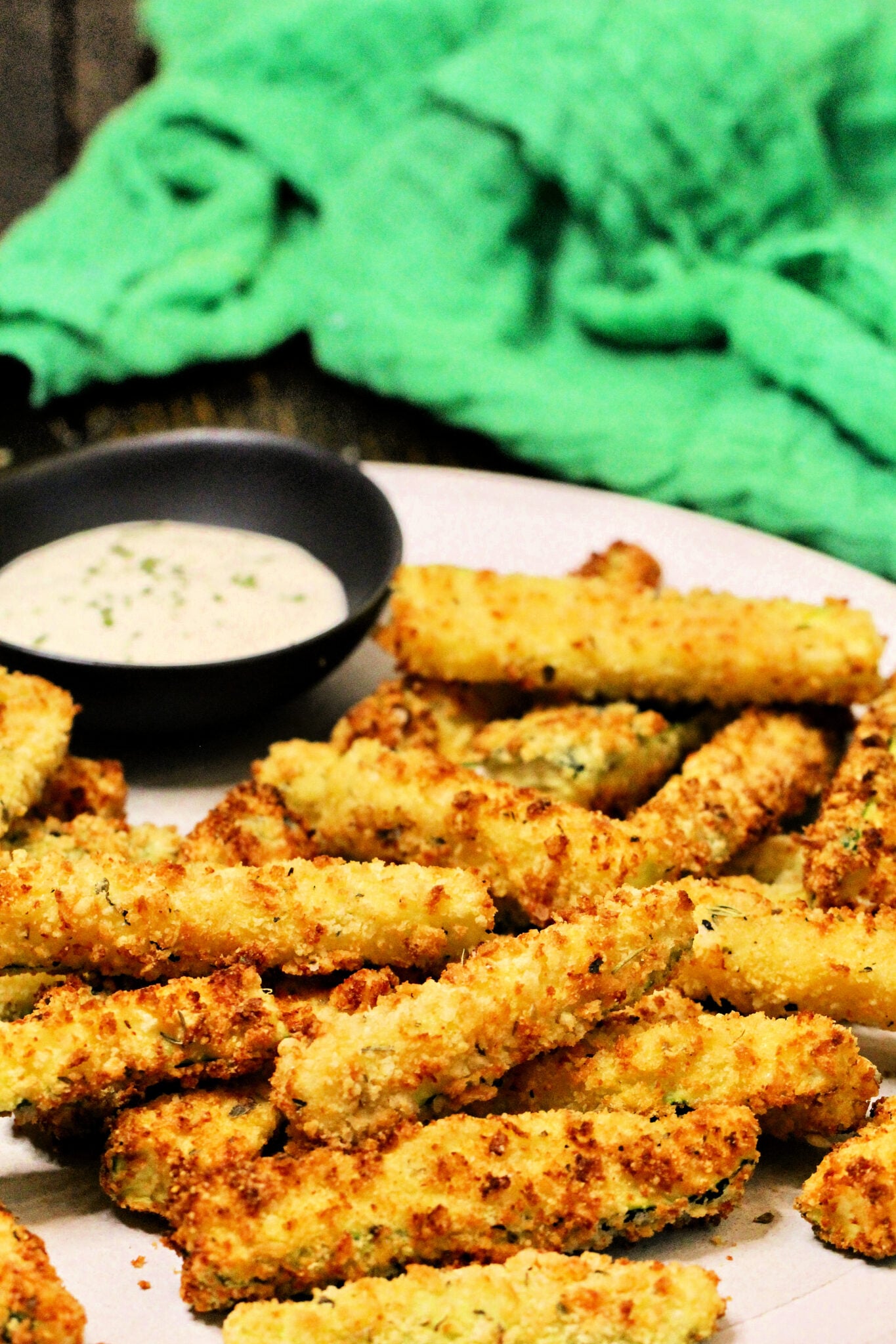 Air fryer zucchini fries on a plate with bowl of ranch dipping sauce and a green napkin.
