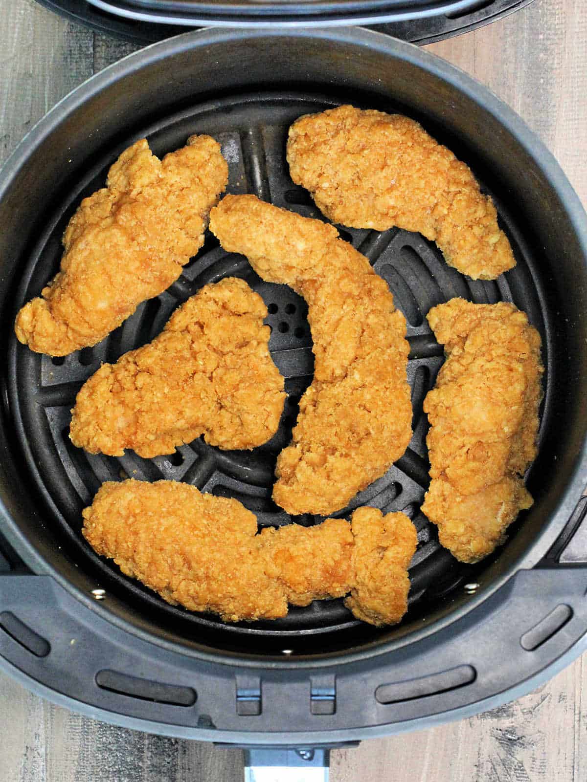 Chicken tenders in air fryer basket.