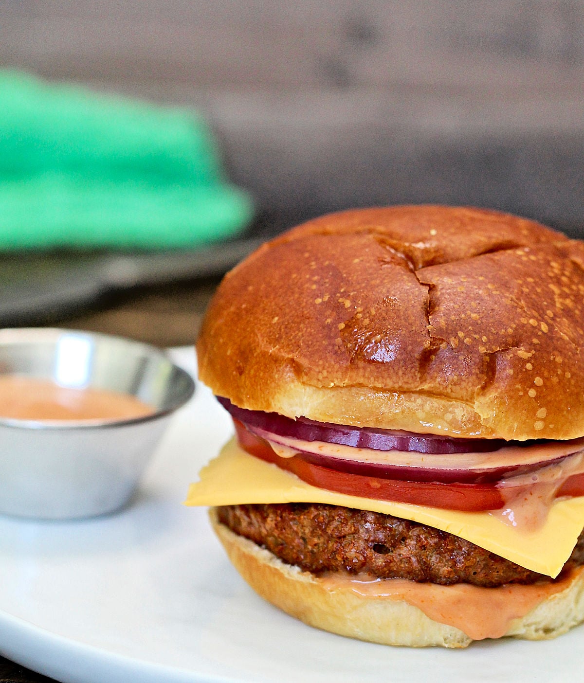Beyond burger on a white plate with burger sauce in a silver bowl on the side and a green napkin in the background. 