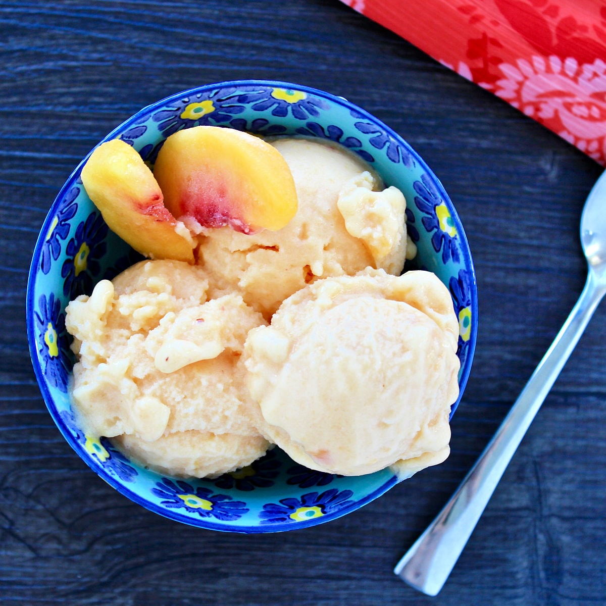 Overhead shot of healthy peach frozen yogurt and two sliced peaches in a blue bowl.