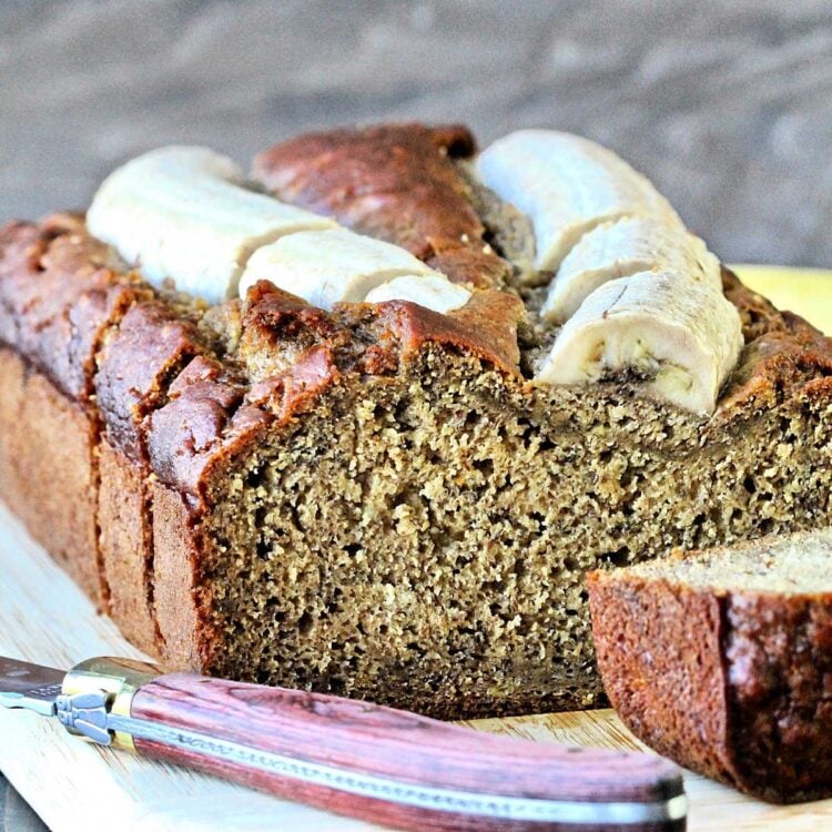 Banana flax bread on a wooden cutting board with a slice cut off.