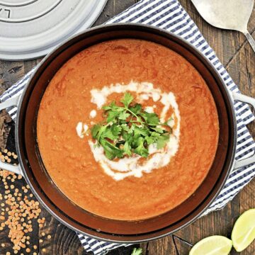 Overhead photo of red lentil coconut soup in a pot garnished with yogurt and cilantro.