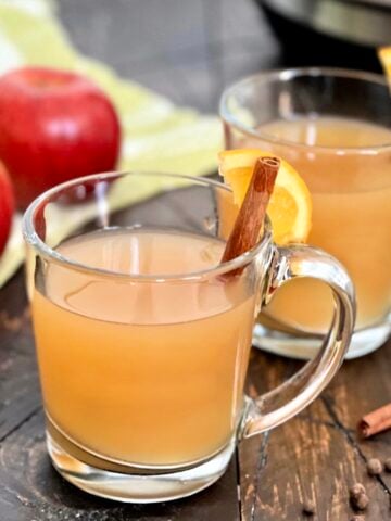 A glass of crock pot mulled cider with a cinnamon stick.
