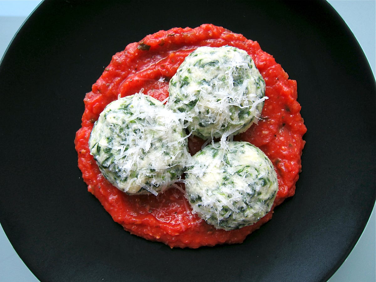 Three spinach gnudi with tomato sauce on a black plate.