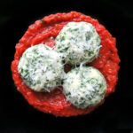 3 spinach gnudi on a black plate.