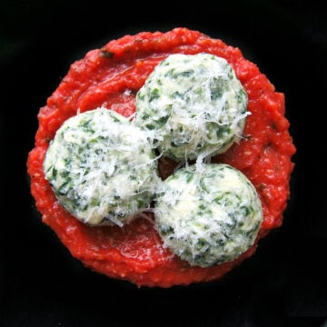 3 spinach gnudi on a black plate.