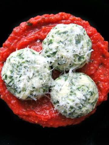 3 spinach gnudi on a black plate.