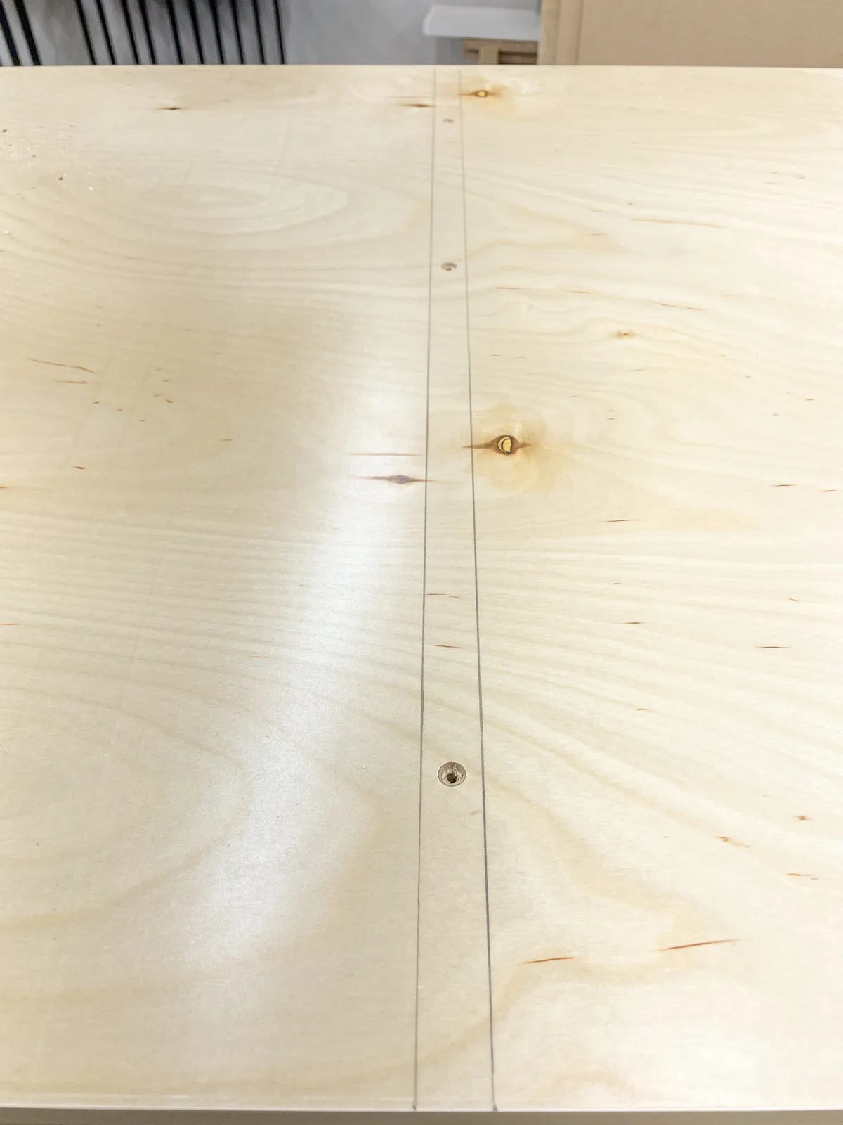 predrilled holes between two marked lines on a sheet of plywood