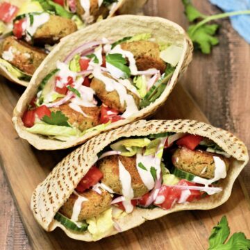 3 falafel pita sandwiches on wood board.