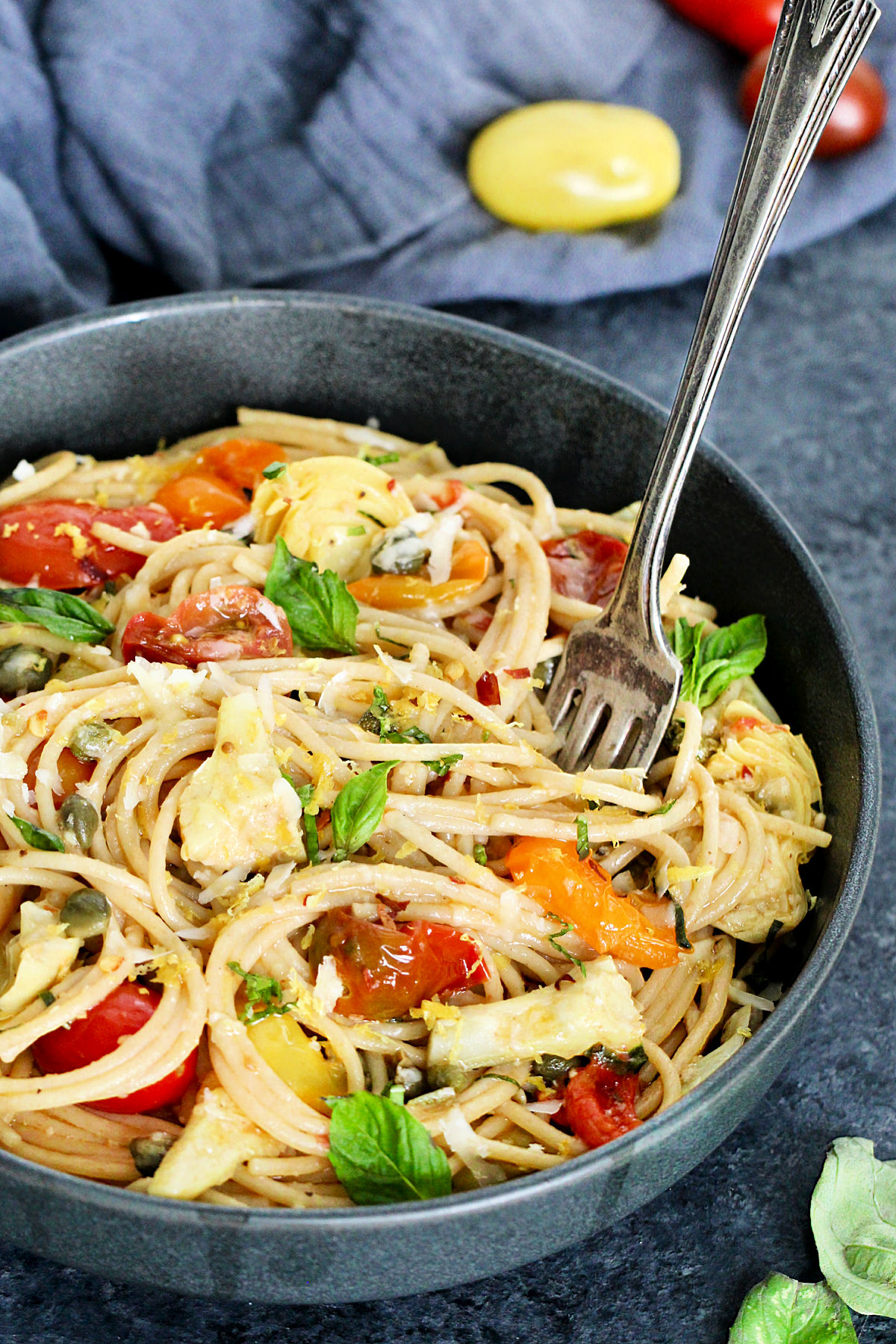 Close up of Mediterranean pasta in a gray bowl with a fork sticking in it.
