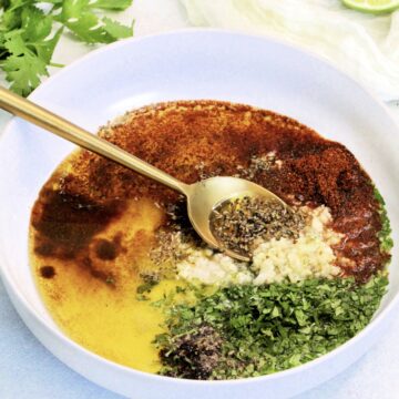 Mexican chicken marinade in white bowl with gold spoon.
