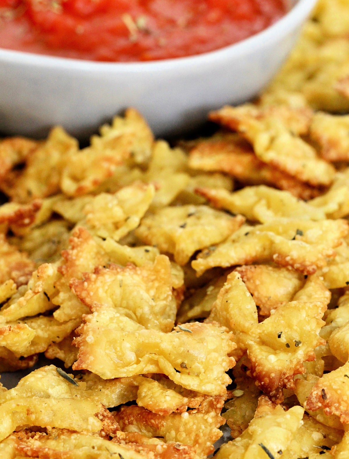 Close up of pasta chips with a bowl of marinara in the background.