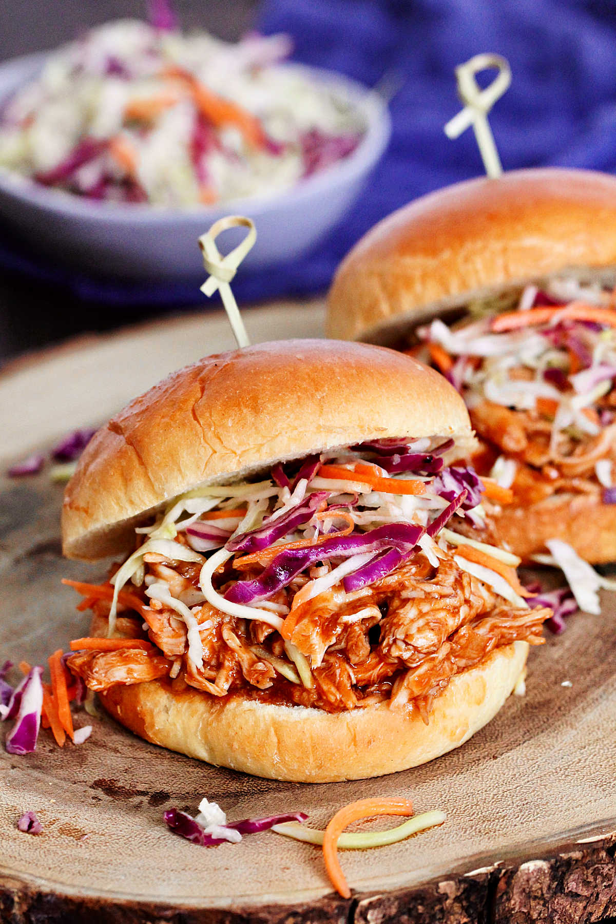 Two pulled chicken sandwiches on a wooden board.