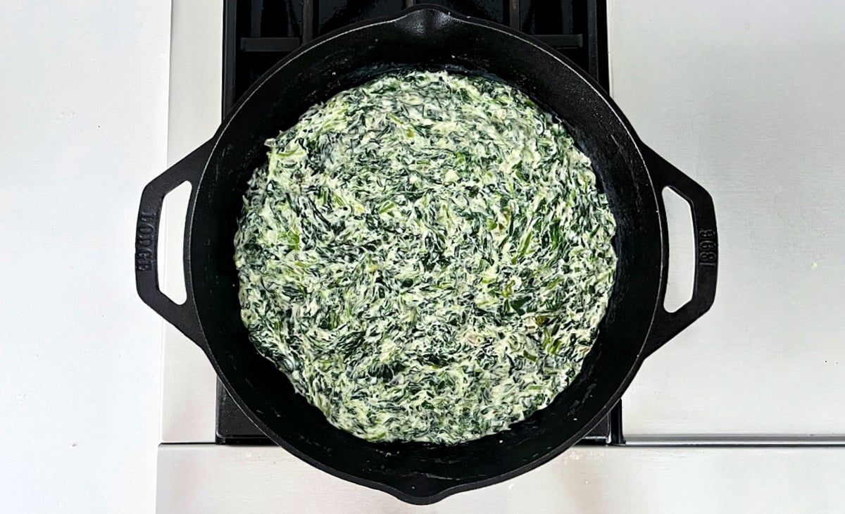 Creamed spinach in a black cast iron skillet on the stove.