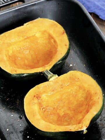 Microwaved acorn squash in a black baking dish with a blue napkin nearby.