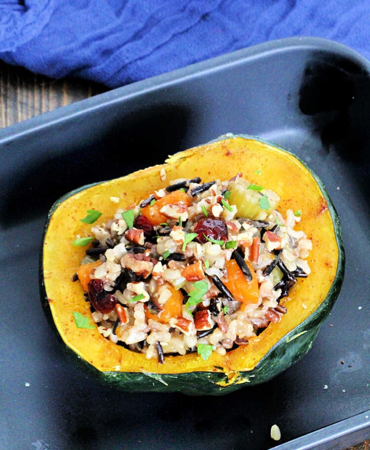 Microwaved acorn squash stuffed with wild rice pilaf in a black baking dish.