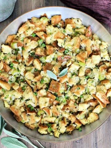 Classic Sage Stuffing in a copper pan with sage, a metal spoon and a brown napkin around it.