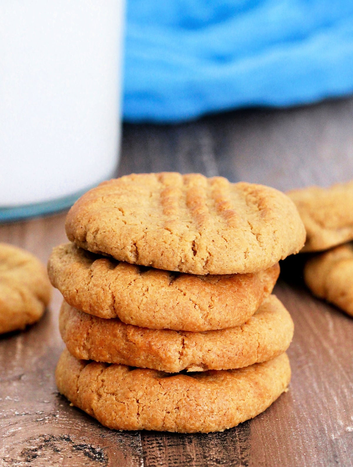 Stack of air fryer peanut butter cookies near a glass of milk and blue napkin.