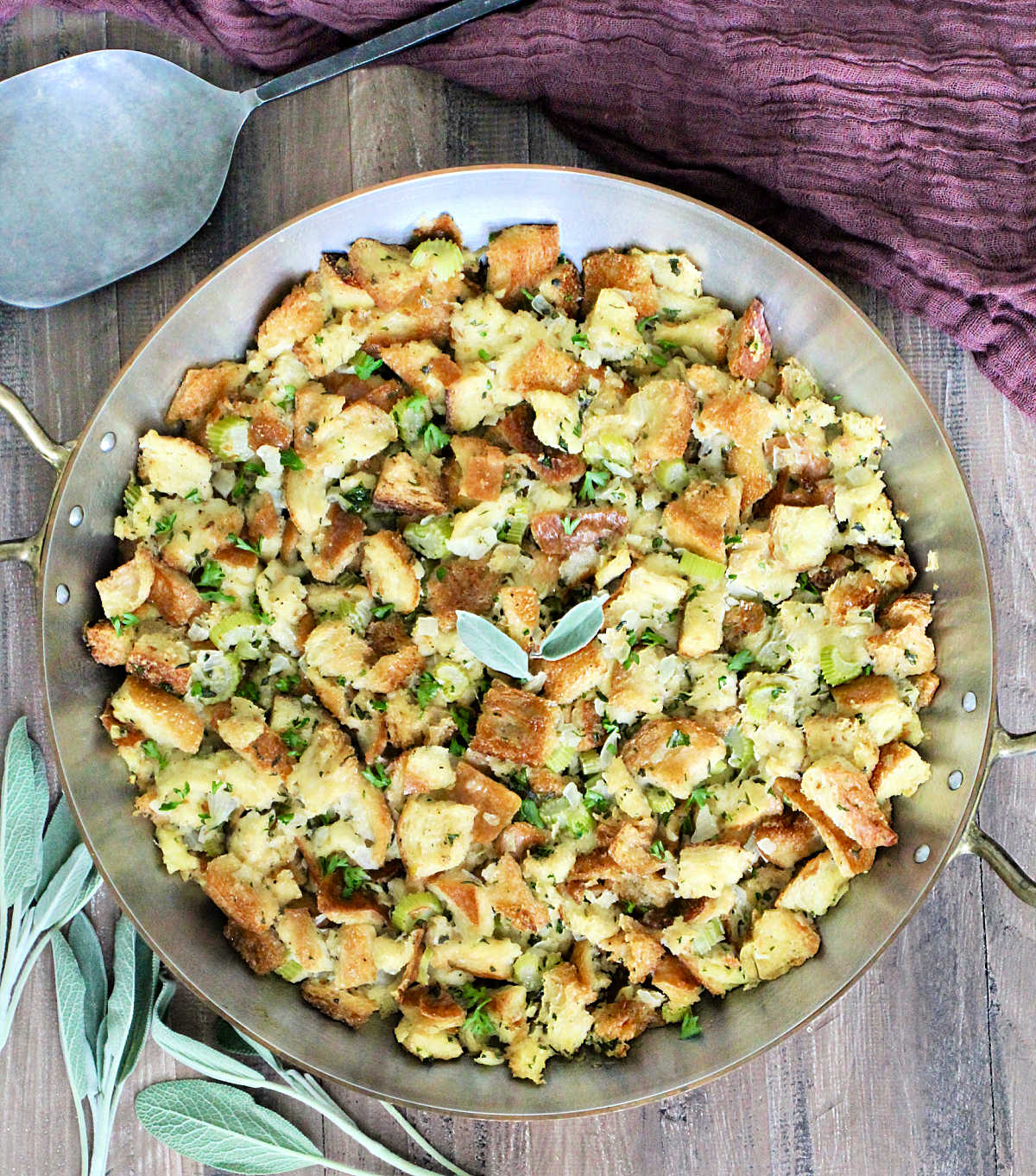 Classic Sage Stuffing in a copper pan with sage, a metal spoon and a brown napkin around it.