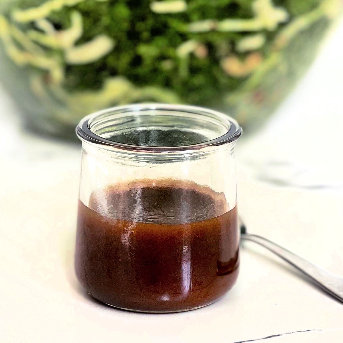Balsamic vinaigrette in a glass jar in front of a salad.