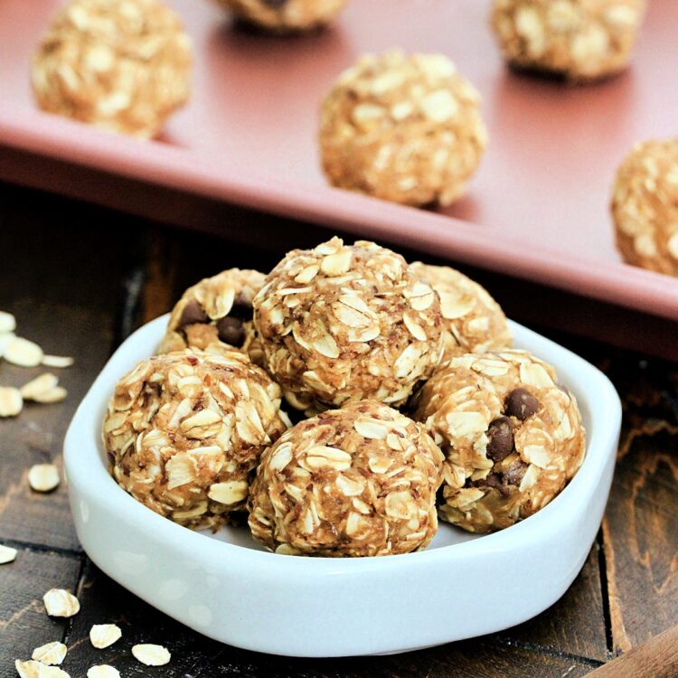 A stack of 3-Ingredient Peanut Butter Oatmeal Balls on a white dish in front of more balls on a pink baking sheet.