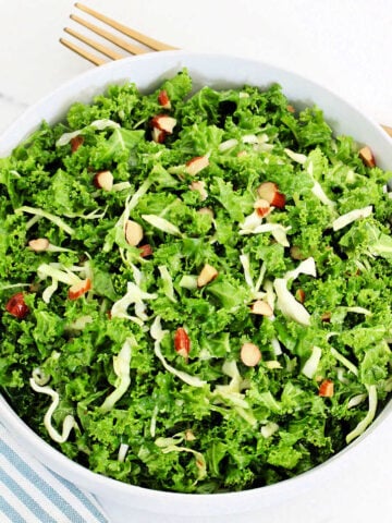 A copycat recipe of Chick-fil-A kale crunch salad in a white bowl with a blue striped napkin and gold fork around it.