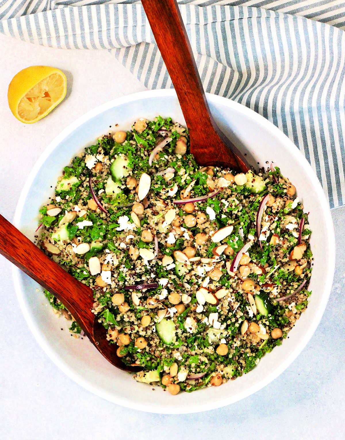 A quinoa and kale salad in a white bowl with a wooden serving spoon and fork.