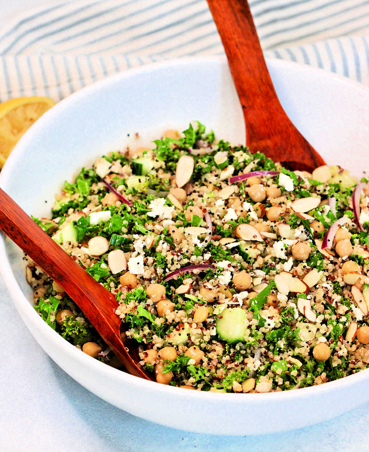 A quinoa and kale salad in a white bowl with a wooden serving spoon and fork.