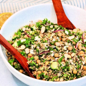 A quinoa and kale salad in a white bowl with a wooden serving spoon and fork.