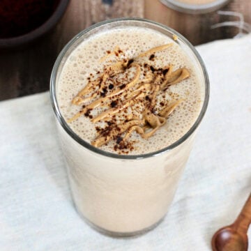 A coffee protein smoothie on a wooden board with a white napkin and a wooden spoon.