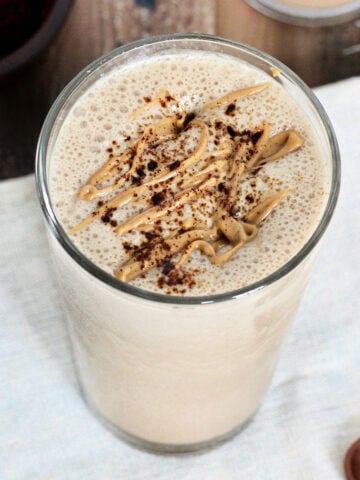 A coffee protein smoothie on a wooden board with a white napkin and a wooden spoon.