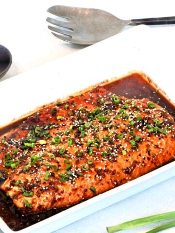 Honey ginger salmon in a white serving platter with sesame seeds and a silver serving utensil in the background.