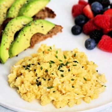 High protein scrambled eggs with cottage cheese on white plate with avocado toast and mixed berries