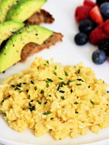 High protein scrambled eggs with cottage cheese on white plate with avocado toast and mixed berries
